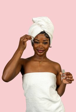 Pembe arka planda izole edilmiş bir pipetle yüzüne su serumu süren mutlu bir müşteri.