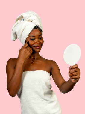 Havlu giyen genç bir kadın duş aldıktan sonra yüzüne Gua sha masaj aleti sürüyor.