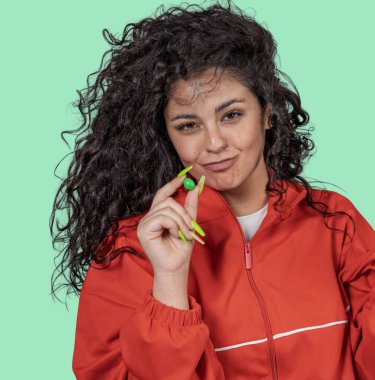 Genç bir kadın parmaklarının arasında yeşil bir şeker tutuyor, neşeli bir şekilde izleyiciye bakıyor, canlı yeşil bir arka planda izole edilmiş.