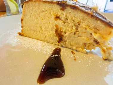 Kremalı peynirli kek dilimi, karamel ve pudra şekeri beyaz tabakta, tadını çıkarmaya hazır.