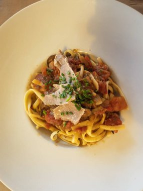 Tagliatelle makarna tabağında ton balığı, domates sosu ve bir tutam taze soğan, beyaz bir kasede servis edilir.