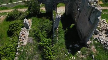 Yeşil çimlerle çevrili, kemerleri ve kırık duvarları olan antik bir binanın kalıntıları.