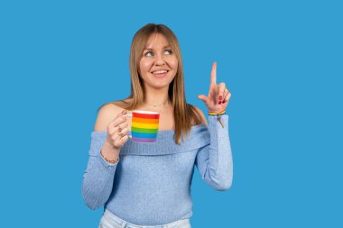 Gökkuşağı bardağını tutan ve gururu ve çeşitliliği kutlamak için parmağını kaldıran genç bir kadının stüdyo fotoğrafı.