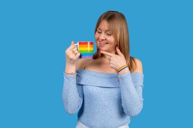 Gökkuşağı kupası ve bileziği gururla sergileyen genç bir kadının stüdyo portresi lgbtq + gurur ve kapsayıcılığı sembolize ediyor.