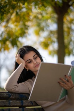Genç bir kadın güzel bir sonbahar gününde parkta bir bankta otururken kitap okumaktan zevk alıyor.