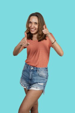 Stüdyo çekimlerinde, turkuaz arka plana parmak doğrultan genç bir kadın görülüyor.