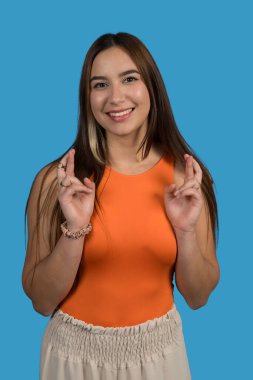 Umut dolu bir gülümseme ile dilek tutan neşeli, genç bir Latin kadının stüdyo portresi.