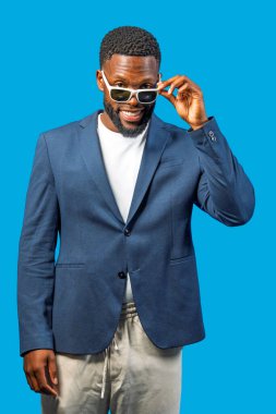Bir iş adamının portresi. Güneş gözlüklerini indiriyor ve mavi bir arka planda gülümsüyor.