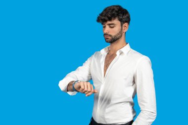 Beyaz gömlekli bir iş adamı mavi arka planda saatine bakıyor.