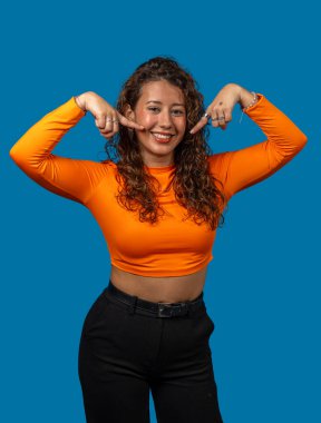 Neşeli genç bir kadının stüdyo portresi canlı mavi bir arka planda gülüşünü gösteriyor.