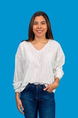 Canlı, mavi bir arka plana el ele poz veren neşeli, genç bir Latin kadının stüdyo portresi.