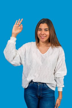 Neşeli genç bir kadının portresi. Mavi arka planda gülümserken işaret veriyor.