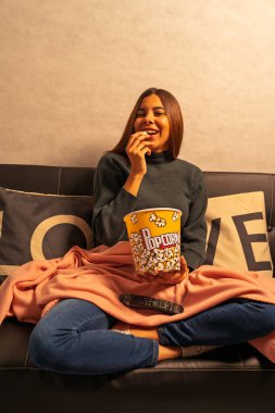 Mutlu kadın kanepede dinleniyor, patlamış mısır yiyor ve film seyrediyor.