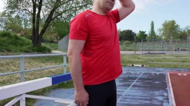 Erkek sporcu kırmızı spor giyer açık havada koşan bir pistte boyun esnetir.