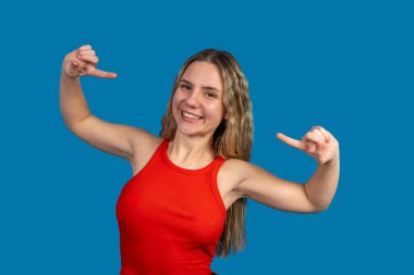 Gülümseyen kadın her iki işaret parmağıyla mavi arka planı işaret ediyor.