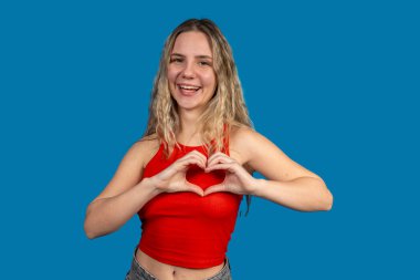 Elleriyle kalbi şekillendiren, sevgi ve pozitifliği ifade eden mutlu genç bir kadın.