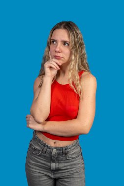 Eli çenesinde genç bir kadın, parlak mavi bir arka plana karşı karar vermeyi düşünüyor.