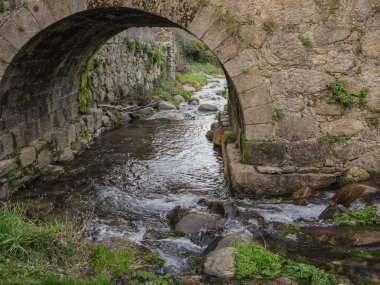 Kırsal alanda antik bir taş köprünün altından akan küçük bir nehir.