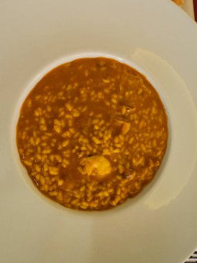 Buharlı deniz ürünleri paella beyaz bir kasede servis edilir, pirinç, karides ve lezzetli bir çorba karışımı sergilenir.