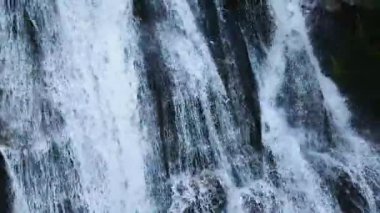 Su, yemyeşil bitki örtüsüyle çevrili kayalık bir arazide güçlü bir şekilde akar.