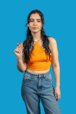 Genç bir kadın, parlak mavi arka planda küçük kırmızı bir nesneyi tutarken parmaklarını şıklatıyor.