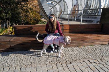 Parktaki bankta oturan kadın örtülü bir palto giymiş köpeğiyle nişanlanıyor.