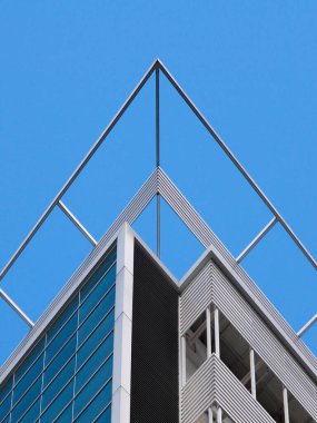 Modern bir binanın kenarı açık mavi gökyüzüne karşı, temiz çizgiler, geometrik şekiller ve mimari minimalizm sergiliyor..