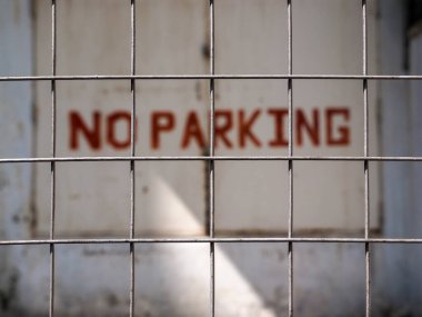 Çelik örgü çitlerin arkasında bulanık bir park yeri tabelası.