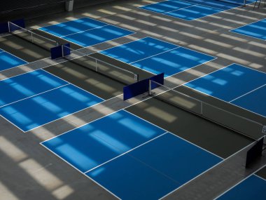 Pickleball sahası mavi servis alanı ve mutfak olarak bilinen koyu gri alan ile kapalı. Voleybol sahasında biraz ışık ve gölgeler var..
