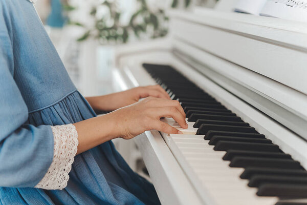 вид сбоку девушки в синем платье, играющей на пианино, руки закрываются. Обучение игре на фортепиано