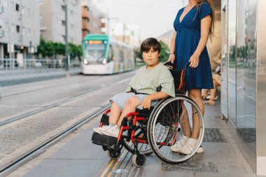 Tekerlekli sandalyeye tutunan genç bir kadın ve içinde oturan güneşi metro istasyonunda hafif bir korkuluk bekliyor.
