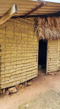 Traditional rustic house made of natural materials such as clay bricks and thatched roof, depicting a rural or indigenous architectural style. The entrance is open, showing the simplicity of the interior. clipart