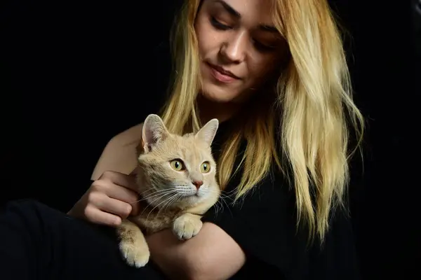 Sarı arka planda sarı bir kedi tutan genç sarışın kadın.