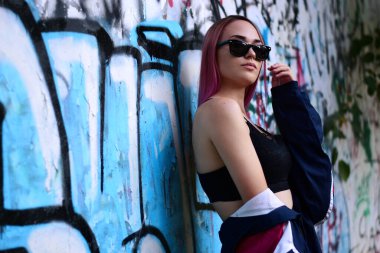 Güneş gözlüklü ve pembe saçlı bir kızın sokak portresi.