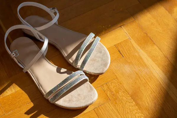 Beyaz, parlak kadın sandaletleri sabah ışığında ahşap zeminde
