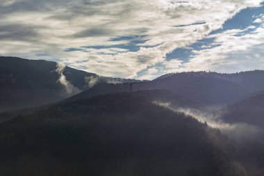 Sabah sisi ve dağların tepelerinde bulutlar, tepenin üstünde gözcü kulesi olan orman manzarası. 