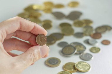 Arka plandaki pek çok madeni paranın önünde 1 euro 'luk bir madeni para tutuyor.