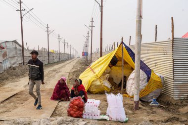  Teneke bir duvarın yanına kurulmuş küçük bir çöp toplayıcı çadırı, Kumbh Mela 'da hareketli bir yol arasında, büyük ruhsal olayı destekleyen görünmeyen işçiyi yansıtıyor..
