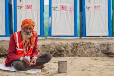 An elderly cleaning worker sits outside the toilets, taking a brief rest amidst the hustle and bustle of Mahakumbh, continuing his dedicated service during the spiritual gathering. clipart