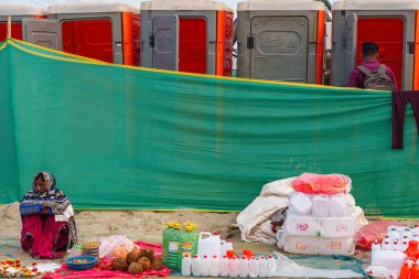 A woman sells water bottles for collecting Ganga Jal in front of the toilets, while a man heads toward the facilities, capturing the blend of spirituality and everyday life at Mahakumbh. clipart