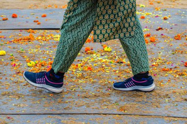 Prayagraj, Uttar Pradesh, Hindistan, 14 Ocak 2025. Sadhus 'un yürüyüşünden sonra yere saçılmış çiçekler, bir kadın patikadan geçerken ayakları görünür..