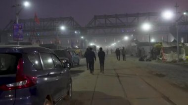 Prayagraj, Uttar Pradesh, Hindistan, 11 Ocak 2025. Demiryolu köprüsünün altında gezen hacıların huzurlu manzarası, geleneği modern mimariyle harmanlıyor..