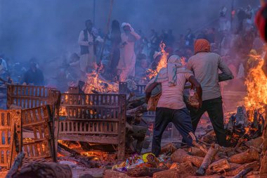 Varanasi, Uttar Pradesh, India, January 26, 2024: Cremation workers at Manikarnika Ghat carry wood, stoke the flames, and perform their tasks with practiced hands, surrounded by smoke and prayers. clipart