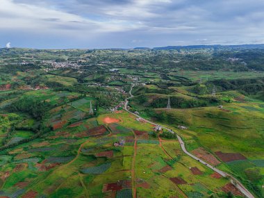 Aerial view of a green meadow, curving mountain road, and a small village covered in misty cloudsperfect for travel and nature visuals. clipart