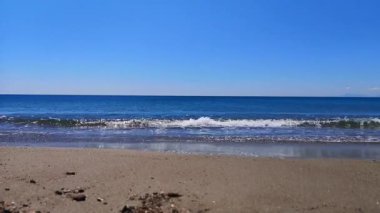 Sakin sahil manzarası: yumuşak dalgalar dalgalı mavi bir gökyüzünün altında kumlu bir sahili sarıyor..