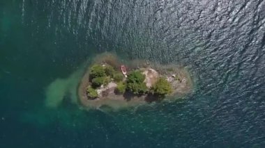 Sakin bir gölde kırmızı bir teknesi olan küçük, tenha bir adanın havadan görünüşü..