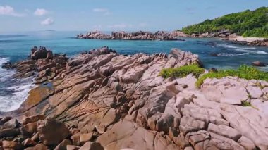 Tropik bir adanın kayalık kıyı şeridini turkuaz suyla sersemleten hava manzarası granit kayalara çarpan dalgalar..