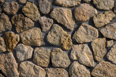 Sıcak tonlu taşlar kırsal bir duvarda mükemmel bir şekilde hizalanır. Gün ortası güneşinin altında parıldar. Doğanın güzelliğini gözler önüne serer..