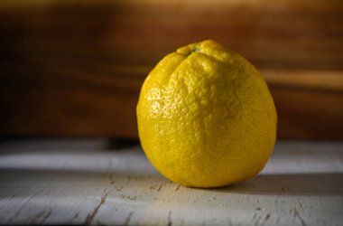 Parlak bir limon, ahşap bir arka planda dokulu tenini sergiliyor ve duyularını tazeliği keşfetmeye davet ediyor..