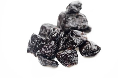 Koyu, buruşuk kuru erikler temiz, beyaz bir zemin üzerinde uzanır, zengin renklerini ve davetkar dokusunu sergilerler..